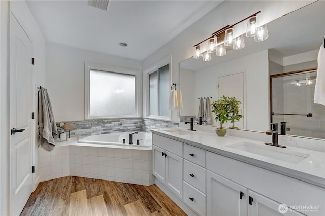 full bath with visible vents, wood finished floors, a garden tub, and a sink