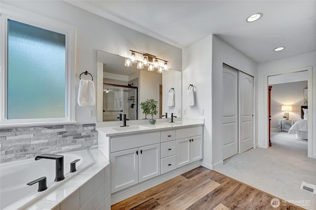 bathroom with a bath, double vanity, wood finished floors, and a sink