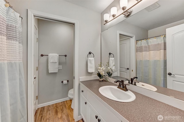 bathroom with baseboards, toilet, wood finished floors, and vanity