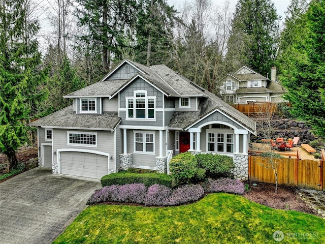 craftsman-style home featuring fence, roof with shingles, an attached garage, concrete driveway, and a front lawn