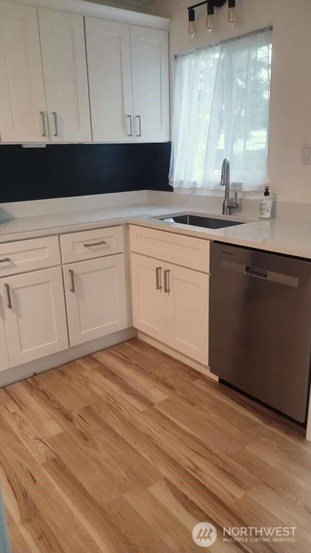 kitchen featuring a sink, stainless steel dishwasher, light wood-style floors, white cabinets, and light countertops