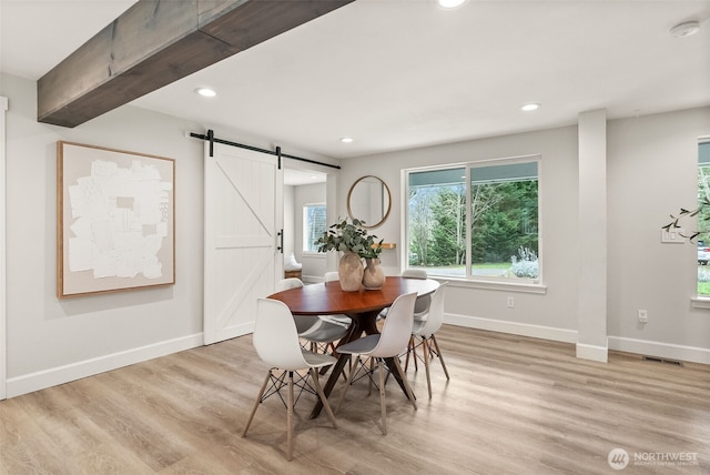 dining area with a barn door, baseboards, visible vents, and light wood finished floors