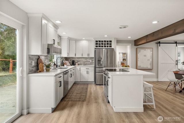 kitchen with a kitchen island, a sink, stainless steel appliances, a barn door, and light wood-type flooring