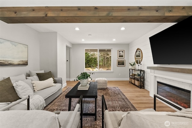 living area featuring beamed ceiling, a glass covered fireplace, recessed lighting, light wood finished floors, and baseboards