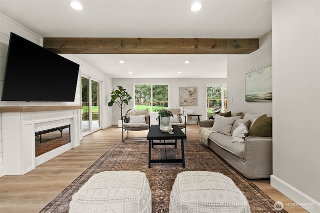 living area featuring baseboards, beamed ceiling, recessed lighting, wood finished floors, and a glass covered fireplace