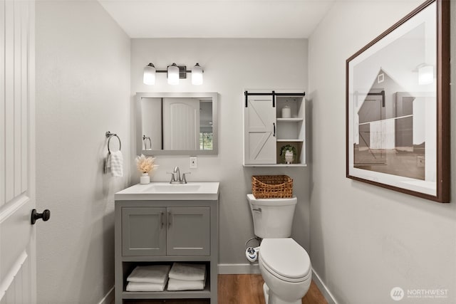 bathroom with vanity, toilet, wood finished floors, and baseboards