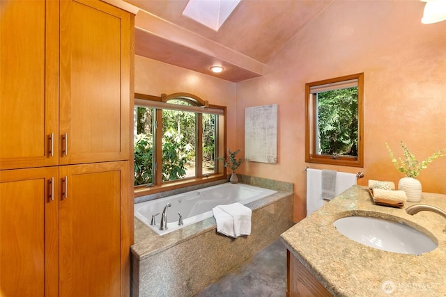 bathroom featuring plenty of natural light, vaulted ceiling with skylight, vanity, and a garden tub