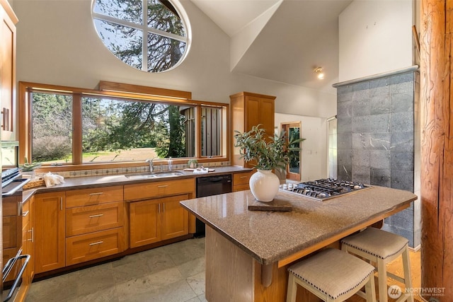 kitchen featuring a warming drawer, a sink, a kitchen breakfast bar, stainless steel gas stovetop, and brown cabinetry