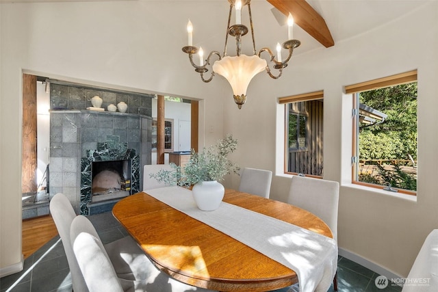 dining room featuring tile patterned floors, beamed ceiling, a notable chandelier, a fireplace, and baseboards