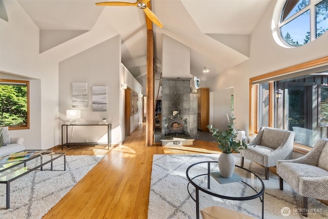 living area with high vaulted ceiling, a wood stove, a ceiling fan, and wood finished floors