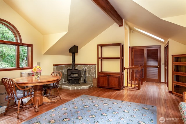 dining room with lofted ceiling with beams, a wood stove, and hardwood / wood-style flooring