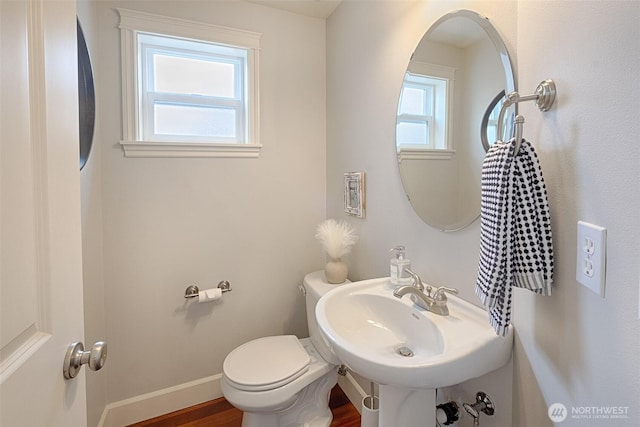 half bath featuring wood finished floors, toilet, baseboards, and a sink