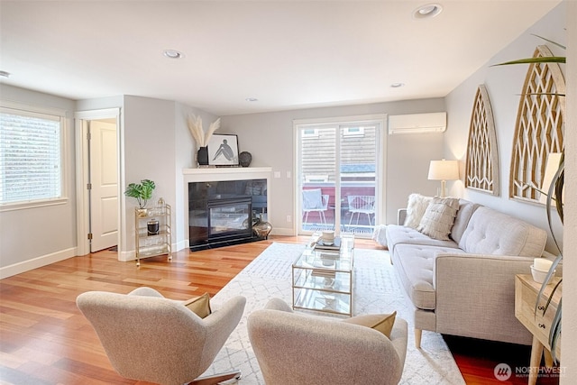 living area featuring plenty of natural light, wood finished floors, baseboards, and a wall mounted air conditioner