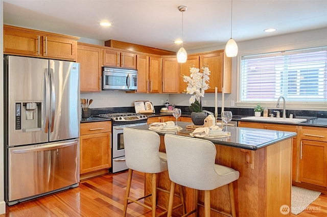 kitchen with a kitchen island, a breakfast bar, light wood-style flooring, a sink, and stainless steel appliances