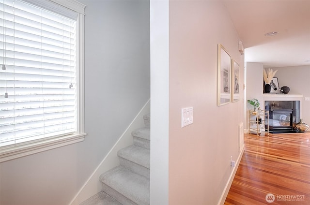 stairway featuring a fireplace, wood finished floors, and baseboards