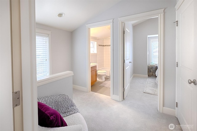 corridor with light carpet, baseboards, and vaulted ceiling