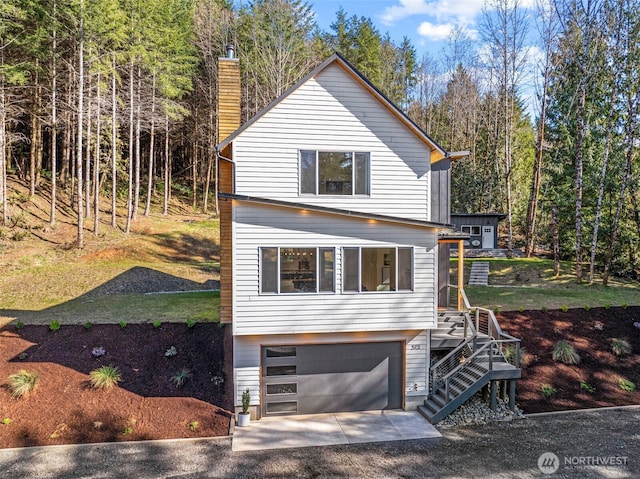 view of front of home with concrete driveway, stairway, an attached garage, and a chimney