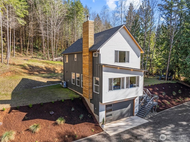 view of home's exterior featuring central AC unit, a chimney, concrete driveway, a garage, and a trampoline