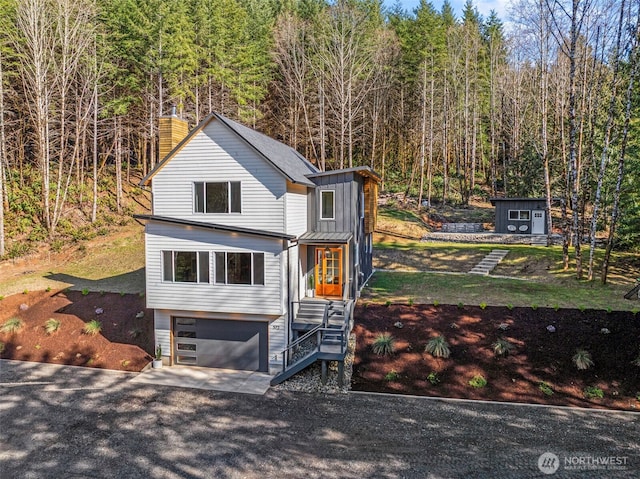 view of front of house featuring an attached garage, a view of trees, and board and batten siding