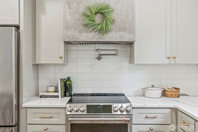 kitchen with light stone counters, decorative backsplash, appliances with stainless steel finishes, and custom range hood