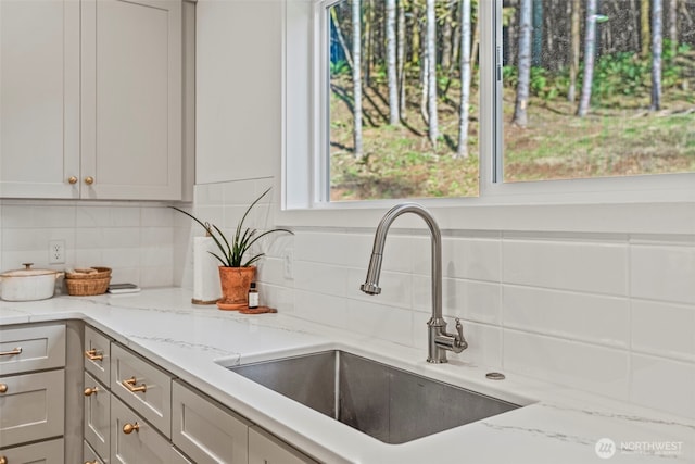 kitchen featuring decorative backsplash, light stone countertops, and a sink