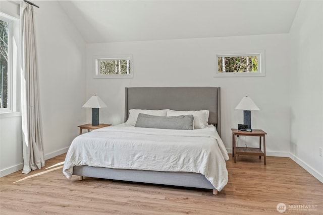 bedroom featuring baseboards, light wood-style floors, and vaulted ceiling