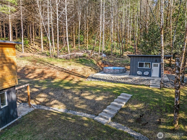 view of yard featuring a forest view, an outdoor fire pit, and an outdoor structure