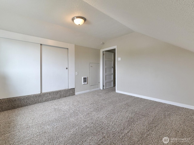 carpeted empty room featuring baseboards, lofted ceiling, a textured ceiling, and heating unit