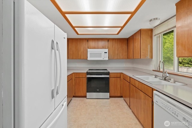 kitchen featuring a sink, white appliances, brown cabinets, and light countertops