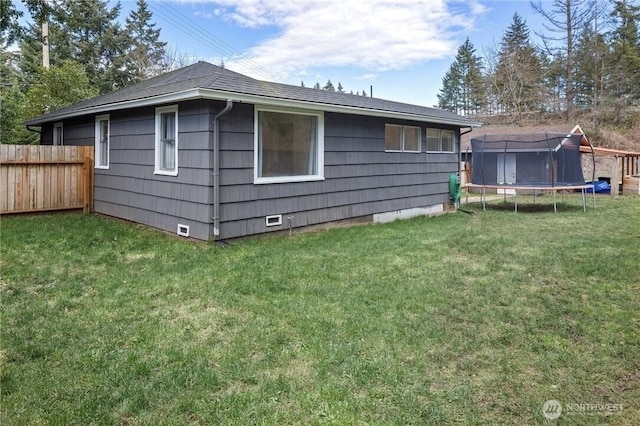 rear view of house featuring crawl space, a trampoline, a lawn, and fence