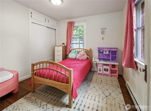 bedroom featuring a closet, wood finished floors, baseboards, and baseboard heating