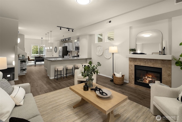 living area featuring baseboards, visible vents, dark wood finished floors, a tile fireplace, and rail lighting