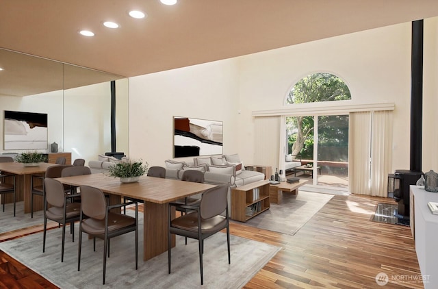 dining space with recessed lighting, a wood stove, light wood-style floors, and a towering ceiling