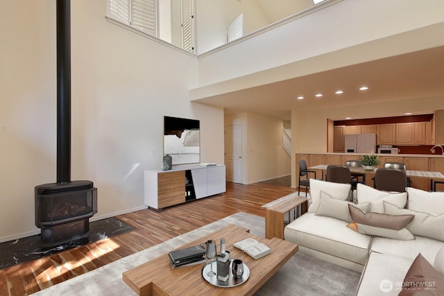 living area featuring baseboards, a high ceiling, a wood stove, recessed lighting, and light wood-type flooring