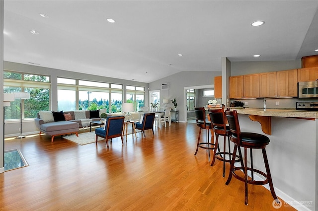 kitchen with a breakfast bar area, light wood-style flooring, light countertops, vaulted ceiling, and stainless steel microwave