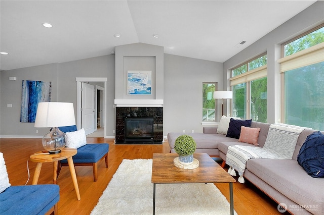 living area with light wood-type flooring, visible vents, lofted ceiling, a premium fireplace, and baseboards