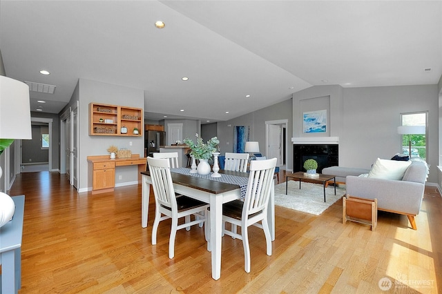 dining area featuring a high end fireplace, visible vents, lofted ceiling, recessed lighting, and light wood-style floors