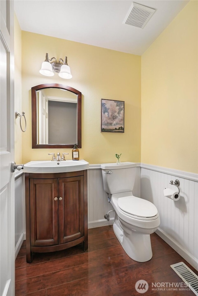 half bath featuring visible vents, toilet, and a wainscoted wall