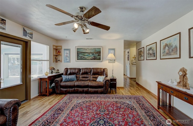 living room featuring visible vents, baseboards, light wood-type flooring, and ceiling fan