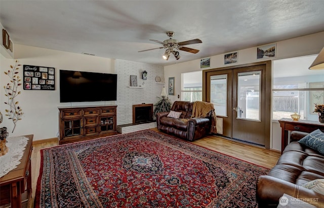 living room featuring visible vents, a brick fireplace, french doors, wood finished floors, and a ceiling fan