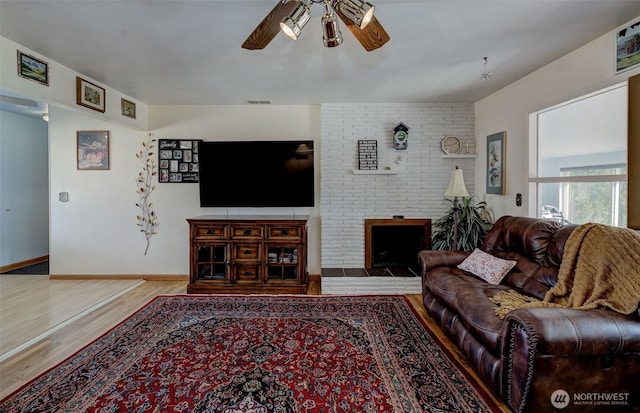 living room featuring visible vents, a ceiling fan, wood finished floors, baseboards, and a brick fireplace