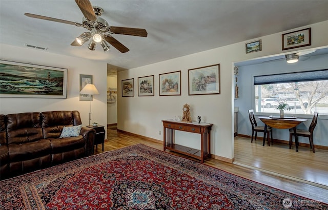 living area featuring a ceiling fan, wood finished floors, visible vents, and baseboards