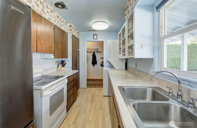 kitchen featuring visible vents, light countertops, freestanding refrigerator, white electric stove, and a sink