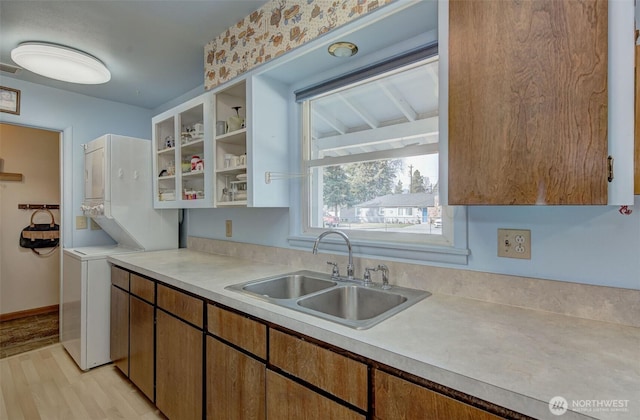 kitchen with a sink, light wood finished floors, stacked washer / dryer, glass insert cabinets, and light countertops