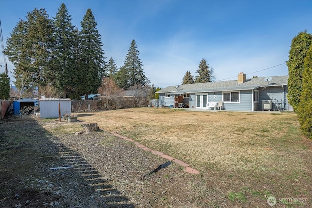 view of yard featuring an outbuilding, french doors, a storage shed, and fence