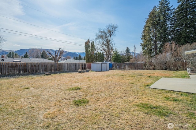 view of yard with a mountain view, an outdoor structure, a fenced backyard, and a storage shed