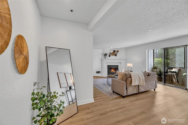 living area with light wood finished floors, a fireplace with flush hearth, a textured ceiling, and baseboards