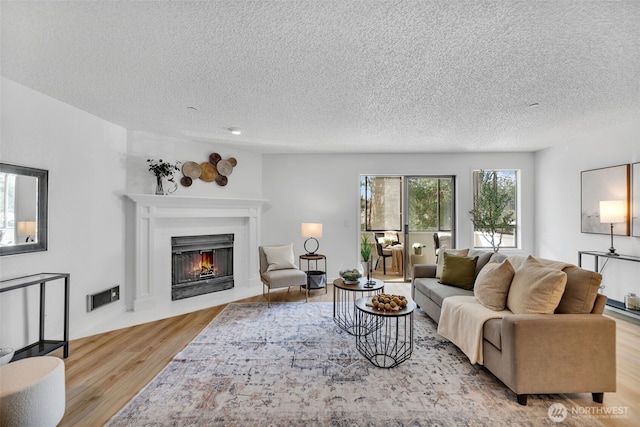 living area featuring a fireplace with flush hearth, visible vents, light wood finished floors, and a textured ceiling