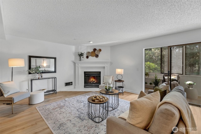 living area with a textured ceiling, wood finished floors, and a lit fireplace