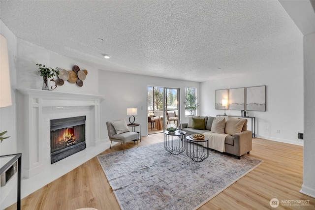 living area with a brick fireplace, a textured ceiling, baseboards, and wood finished floors